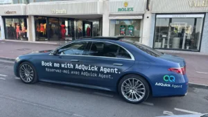 Berline Mercedes Classe S bleu nuit floquée AdQuick Agent stationnée sur la Croisette à Cannes devant les boutiques de luxe Rolex et Valentino, illustrant un service de chauffeur privé pour entreprise.
