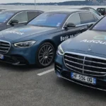 Alignement de quatre berlines de luxe Mercedes Classe S bleu nuit floquées du logo AD QUICK sur un parking en bord de mer, illustrant un service de chauffeur privé pour entreprise haut de gamme.