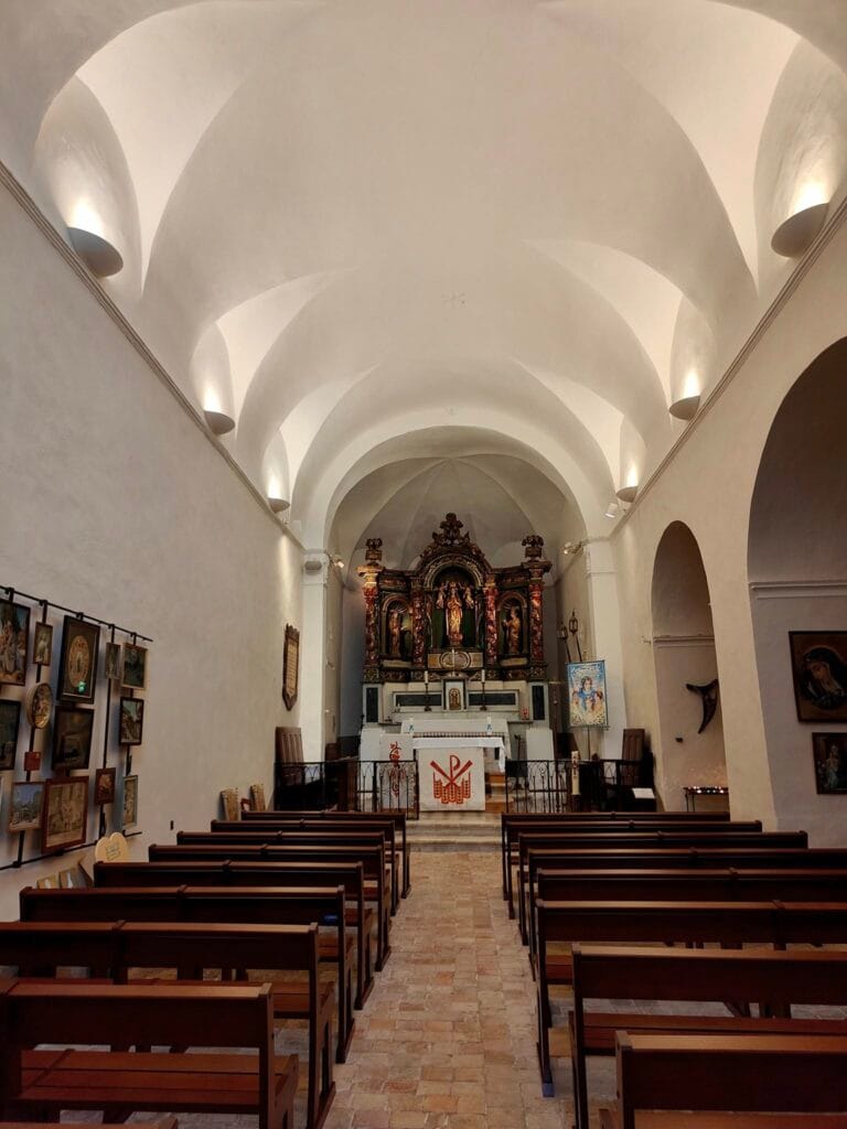 This is the interior of the parish church in the Old Village, built in the Middle Ages and remodeled in the 19th century. It is characterized by its vaulted ceilings, stone walls, and the atmosphere of a small Provençal church. It is located on Rue de l'Église.