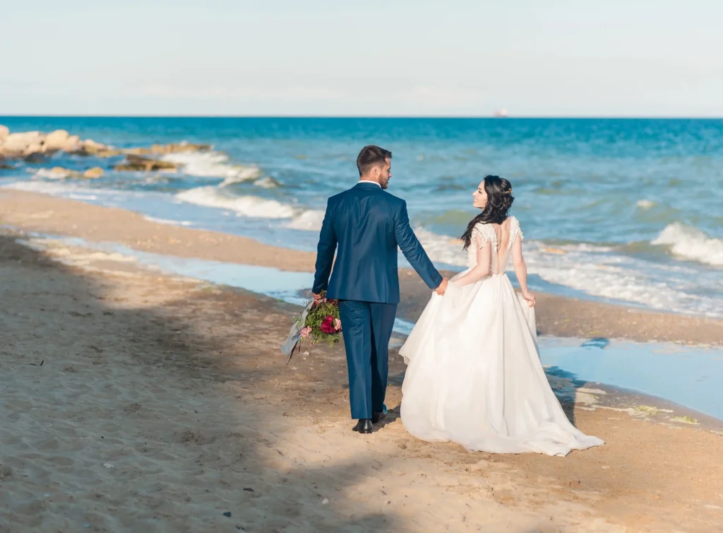 Mariés se tenant la main et marchant le long du rivage sur la plage lors d'un mariage en bord de mer Côte d’Azur.