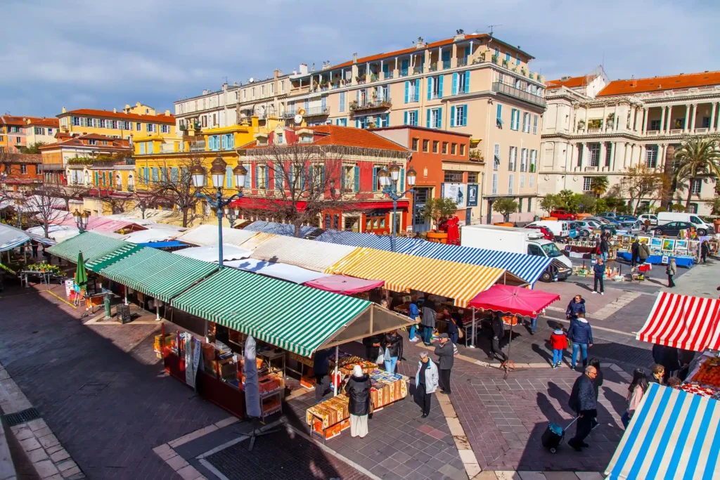 Alignement de stores en toile à rayures rouges, jaunes et vertes au-dessus des étals du marché du Cours Saleya à Nice.