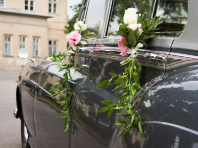 Petits bouquets de roses blanches et roses avec feuillage accrochés aux poignées d'une voiture ancienne pour une décoration voiture des mariés élégante.