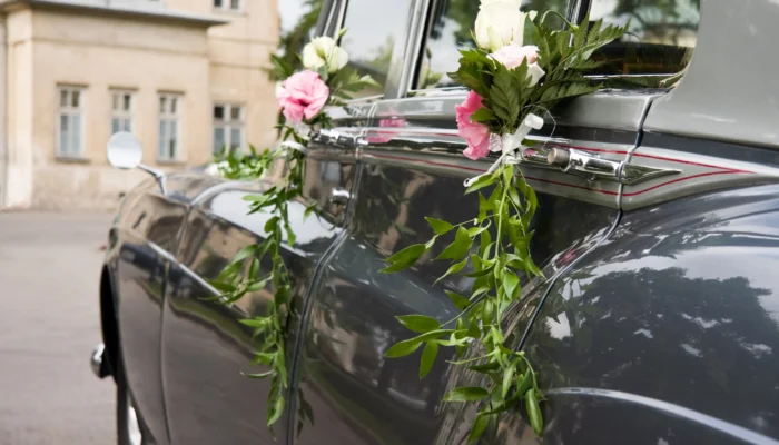 Petits bouquets de roses blanches et roses avec feuillage accrochés aux poignées d'une voiture ancienne pour une décoration voiture des mariés élégante.