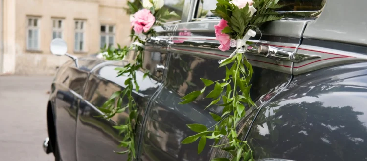 Petits bouquets de roses blanches et roses avec feuillage accrochés aux poignées d'une voiture ancienne pour une décoration voiture des mariés élégante.