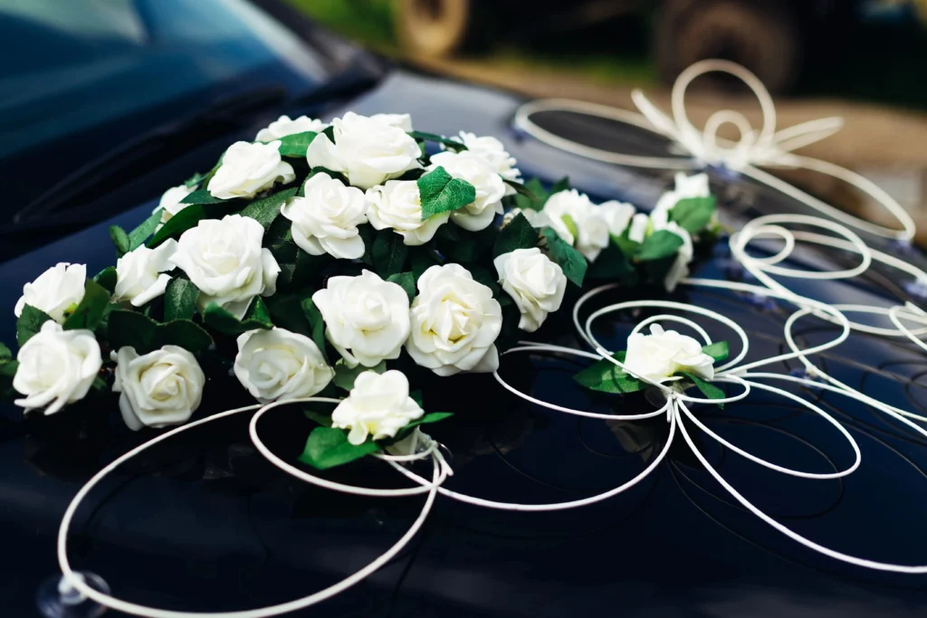 Gros bouquet de roses blanches et rubans entrelacés fixés sur le capot d'une voiture sombre pour une décoration voiture des mariés romantique.