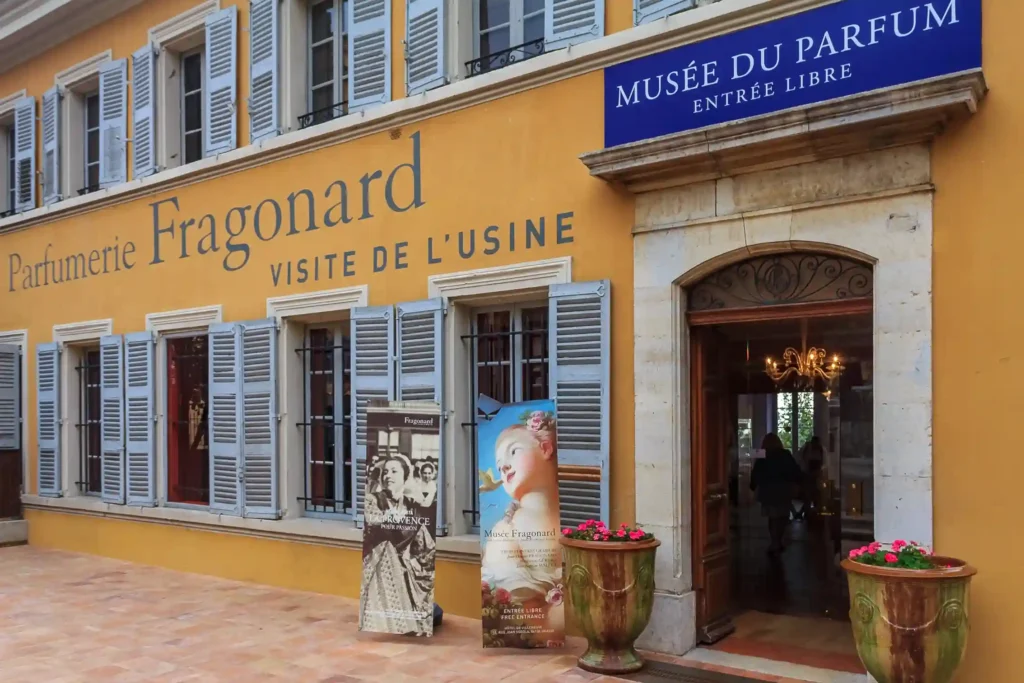 Façade provençale ocre jaune de l'usine historique de la Parfumerie Fragonard, avec ses fenêtres à volets gris bleutés.