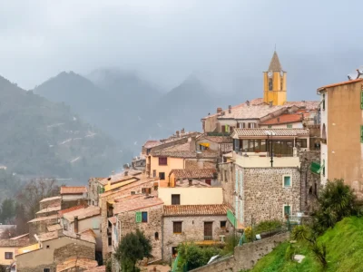 Village perché de Sainte-Agnès avec ses maisons en pierre, son clocher jaune et les montagnes environnantes sous un ciel brumeux.