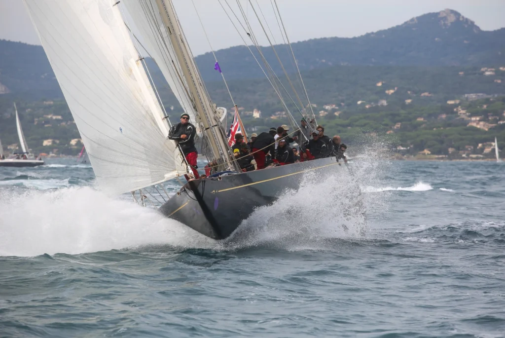 Une vue rapprochée et dynamique d’un grand voilier moderne à coque noire fendant les vagues.
