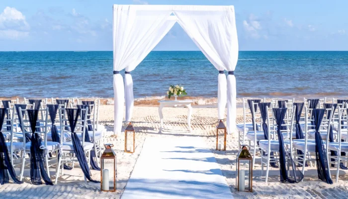 Arche de mariage en voile blanc et chaises d'invités installées sur le sable blanc face à la mer pour un mariage en bord de mer Côte d’Azur.