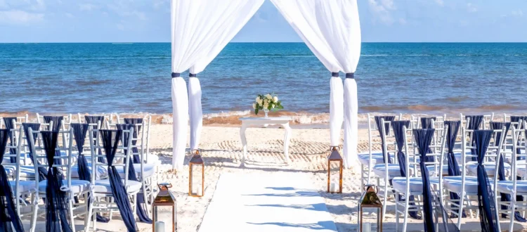 Arche de mariage en voile blanc et chaises d'invités installées sur le sable blanc face à la mer pour un mariage en bord de mer Côte d’Azur.