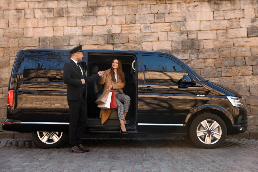 Chauffeur privé accueillant une cliente sortant d'un van haut de gamme, illustrant les avantages VTC.
