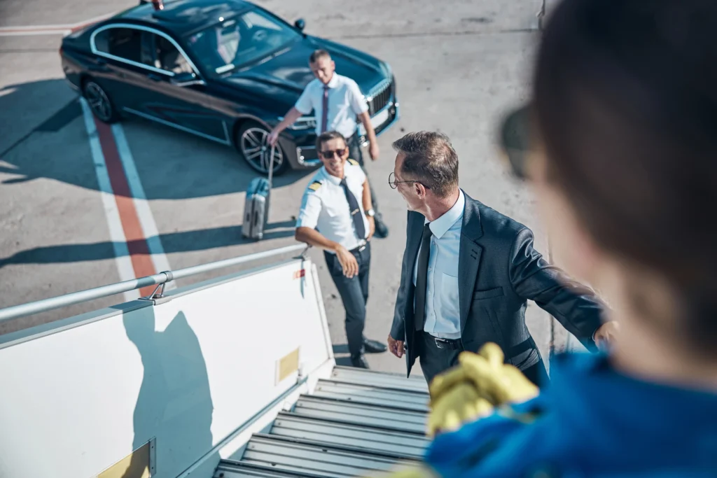 Un chauffeur privé VIP accueillant un homme d'affaires au pied d'un jet privé à côté d'une berline de luxe sur le tarmac d'un aéroport.