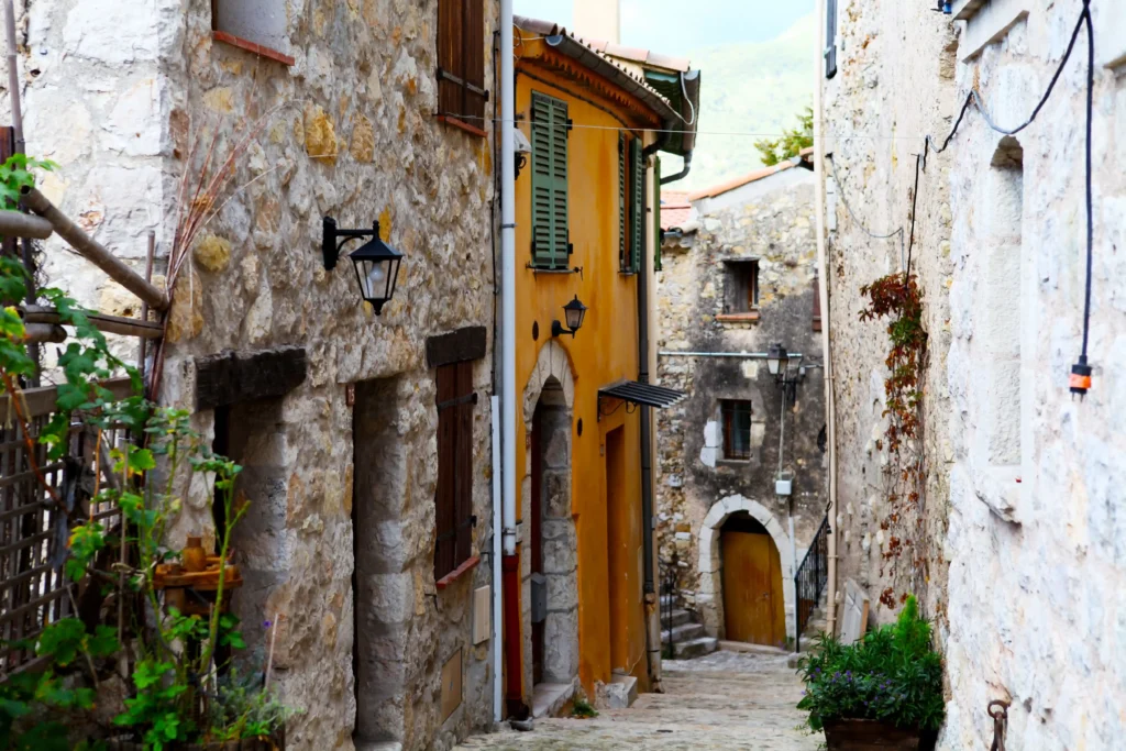 Ruelle médiévale du village de Sainte-Agnès avec maisons en pierre, façade ocre jaune et volets provençaux.