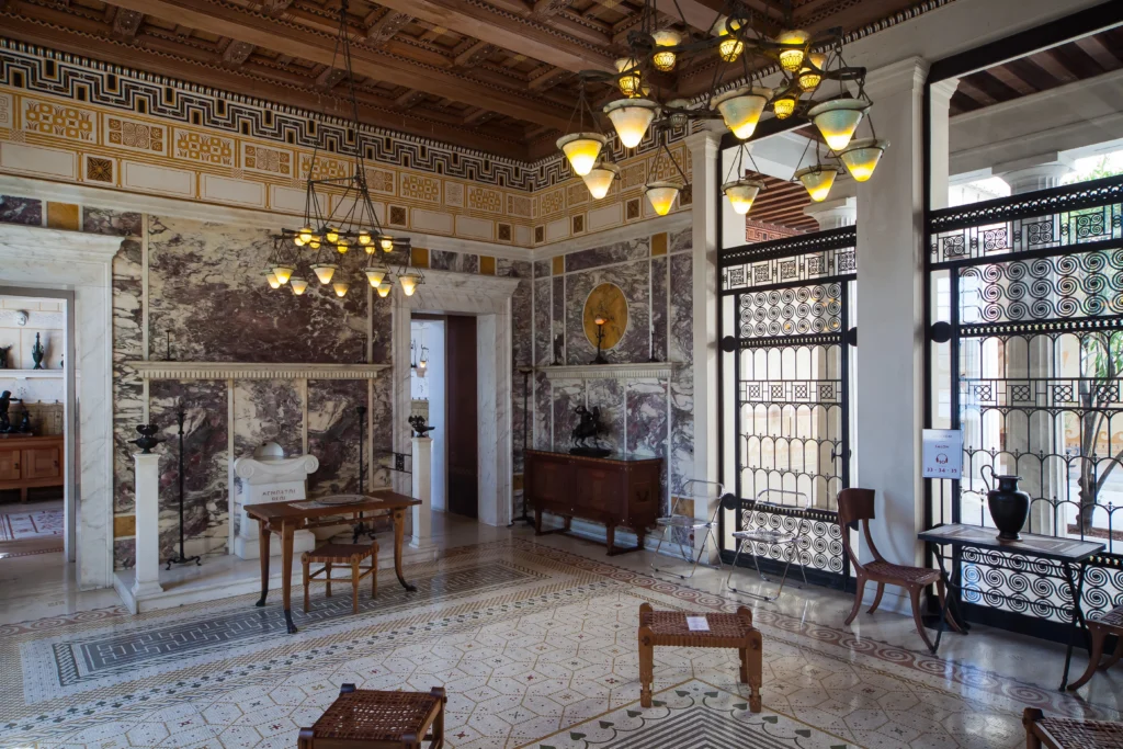 Intérieur luxueux du grand salon de la Villa Kérylos, décoré de marbre violet, de mosaïques au sol, de fresques grecques antiques et de lustres en bronze.