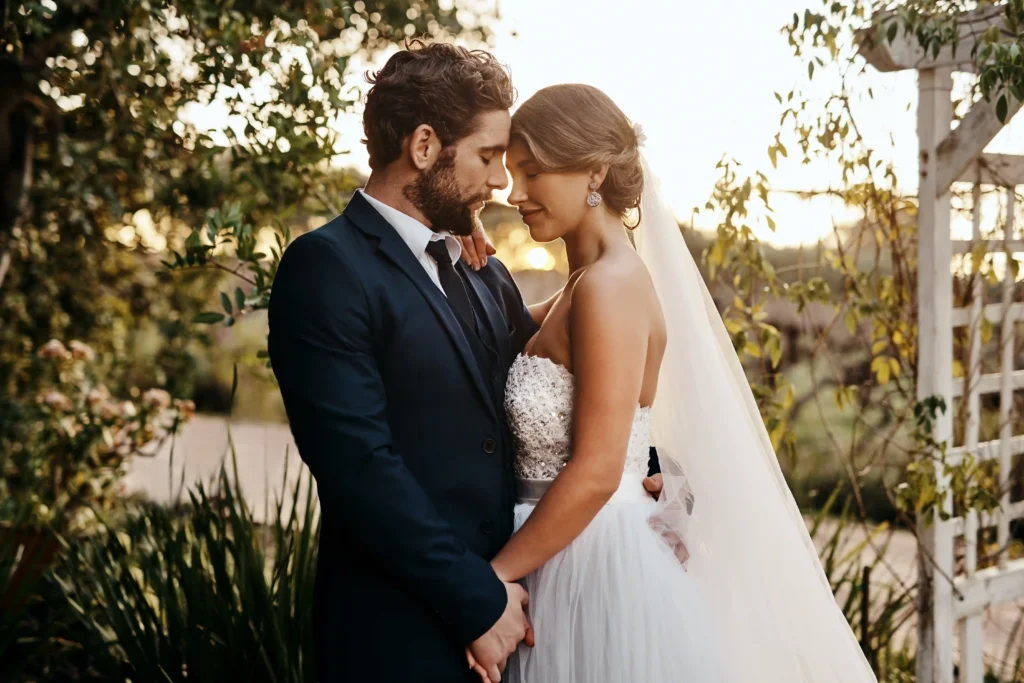 Mariés enlacés dans un jardin romantique au coucher du soleil après avoir réservé une formule de location de limousine avec chauffeur privé pour mariage.