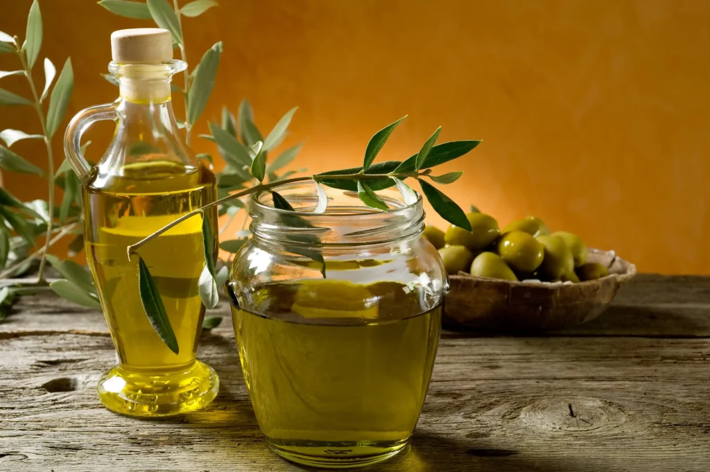 Huile d'olive extra vierge de Provence présentée dans une carafe en verre et un bocal sur une table en bois rustique, accompagnée de branches d'olivier et d'un bol d'olives vertes.