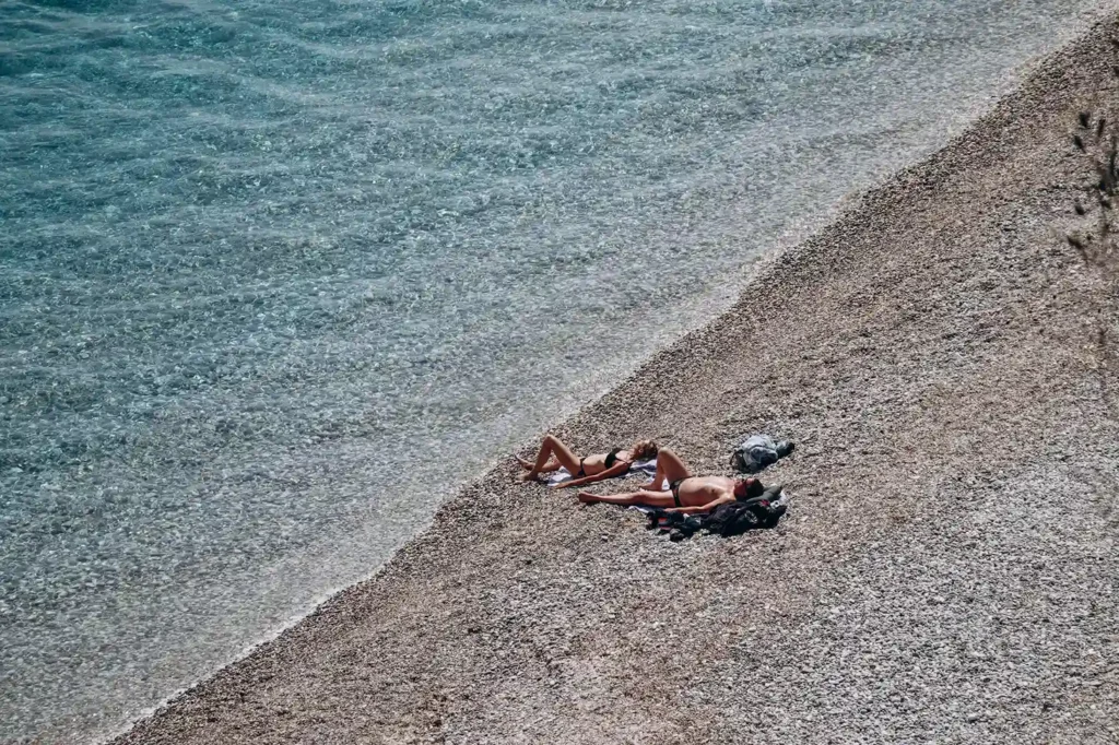 Vue aérienne de deux personnes bronzant sur une plage de galets aux eaux cristallines à Roquebrune-Cap-Martin.
