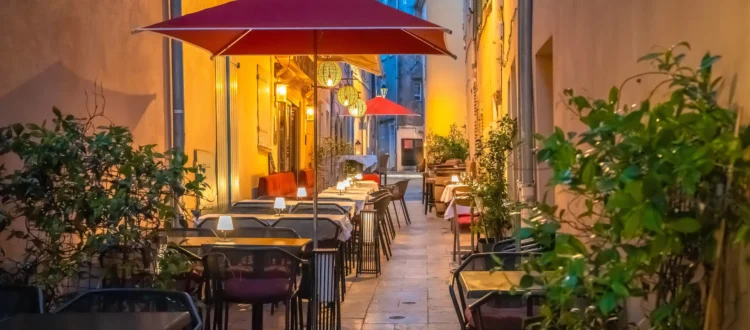 Terrasses de restaurants à Saint-Tropez installées dans une ruelle pittoresque aux façades ocre, éclairées par des lanternes chaleureuses en soirée.