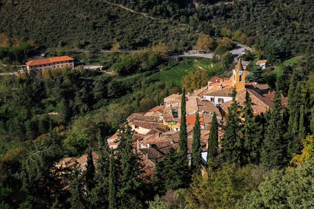 Vue aérienne du village perché de Sainte-Agnès entouré d'une nature verdoyante avec son clocher jaune et ses toits en tuiles.