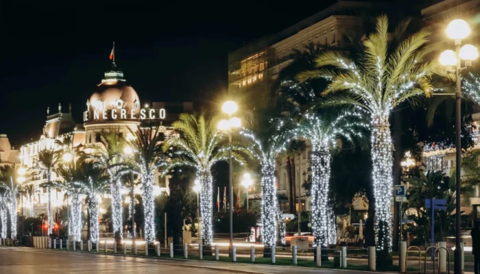 Promenade des Anglais à Nice illuminée la nuit avec des palmiers décorés et des lumières festives de Noël, reflétant la tradition de Noël locale.