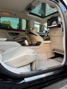 Intérieur luxueux en cuir blanc d'une Mercedes-Maybach Classe S avec écrans vidéo, toit panoramique et éclairage d'ambiance LED pour un service de chauffeur privé pour entreprise.