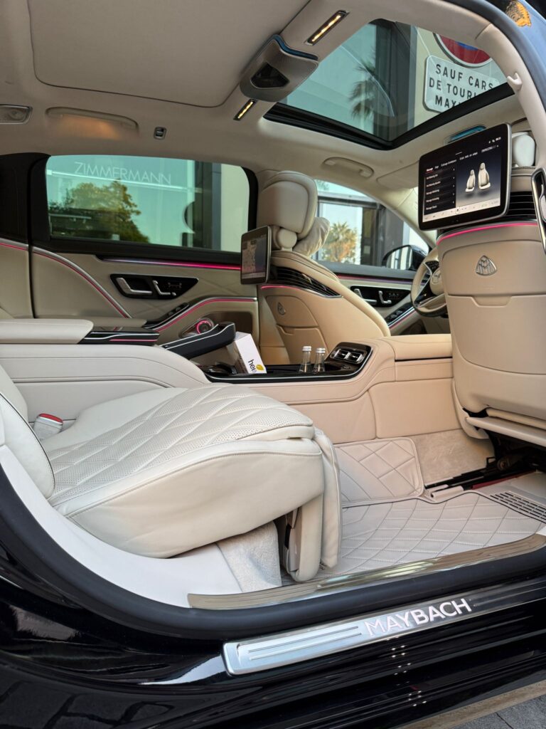 Intérieur luxueux en cuir blanc d'une Mercedes Maybach avec chauffeur privé pour mariage, sièges arrière grand confort, écrans multimédias et éclairage d'ambiance rose.