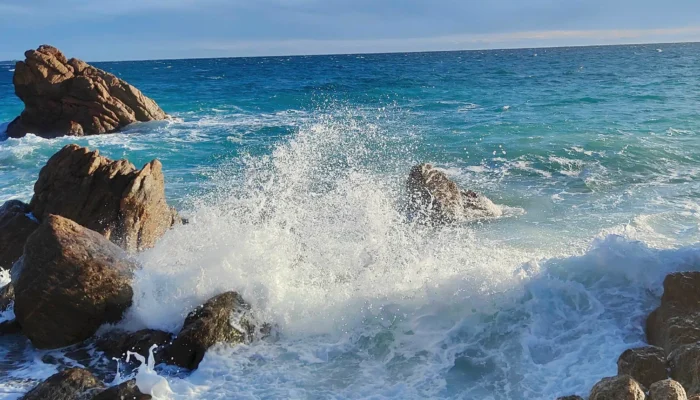 Vue de la Plage des Rochers à Cannes La Bocca montrant les formations rocheuses ocre rouge, le sable fin et l'eau cristalline de la Méditerranée avec le massif de l'Estérel en arrière-plan. @jeanpaul 2025