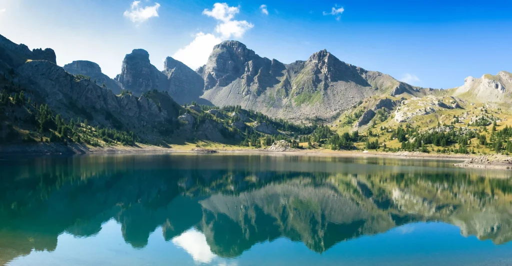 Vue panoramique du Lac d'Allos dans le Parc National du Mercantour. Les eaux bleu profond du lac reflètent les sommets rocheux des Tours d'Allos sous un ciel dégagé. Paysage de haute montagne sauvage et préservé des Alpes-de-Haute-Provence à 2230 mètres d'altitude.
