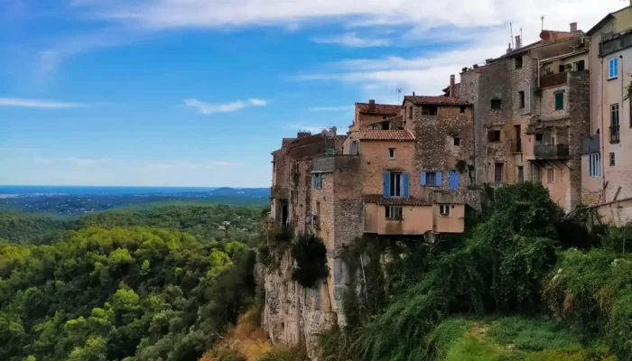 Panoramic view of the medieval village of Tourrettes-sur-Loup, perched on its cliff above a vast green valley of olive groves, under a spectacular cloudy sky. A luxury private car tour destination on the French Riviera. @jeanpaul 2025