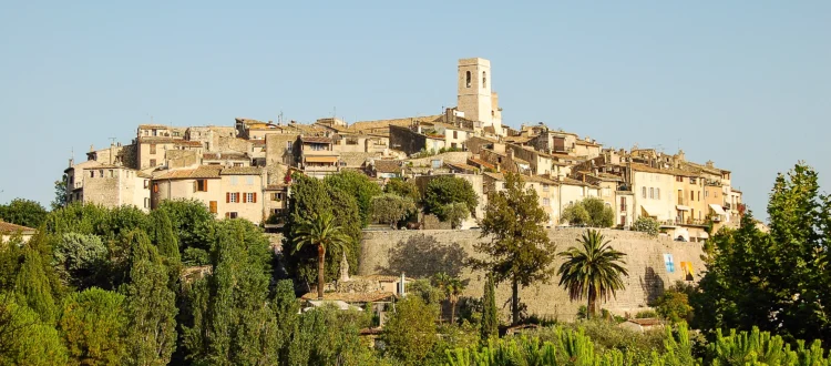 Vue panoramique de Saint-Paul-de-Vence perché sur sa colline, avec ses imposants remparts de pierre dorée entourant le village médiéval, sous la lumière éclatante du soleil provençal.