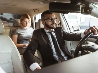 Chauffeur VTC conduisant une dame élégante à Cannes sur la Croisette, berline noire de luxe.