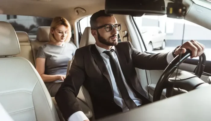 Chauffeur VTC conduisant une dame élégante à Cannes sur la Croisette, berline noire de luxe.