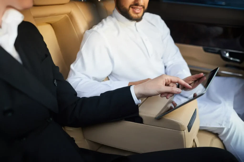 A businessman and a businesswoman being driven by a private chauffeur in a luxury vehicle